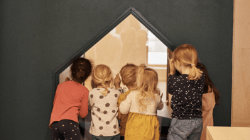 Children peek out of an indoor window at HEI Schools