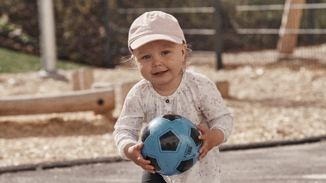 a child holds a soccer ball in hand, looking happy